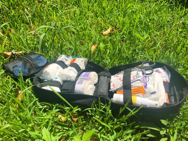 A Molle Shop Individual First Aid Kit Pouch open on the grass, revealing its contents including bandages, gauze, and scissors.