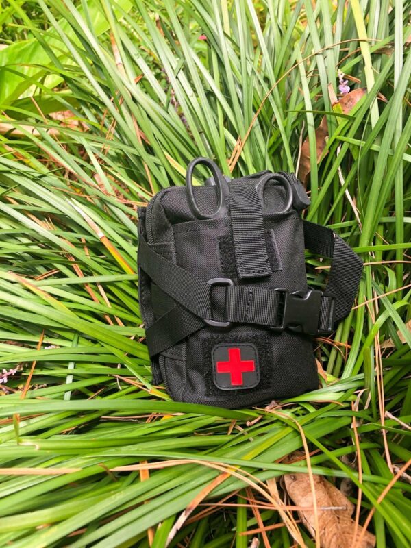 A black Hiking First Aid Kit Bundle with a red cross emblem lying on green grass, perfect for hiking.